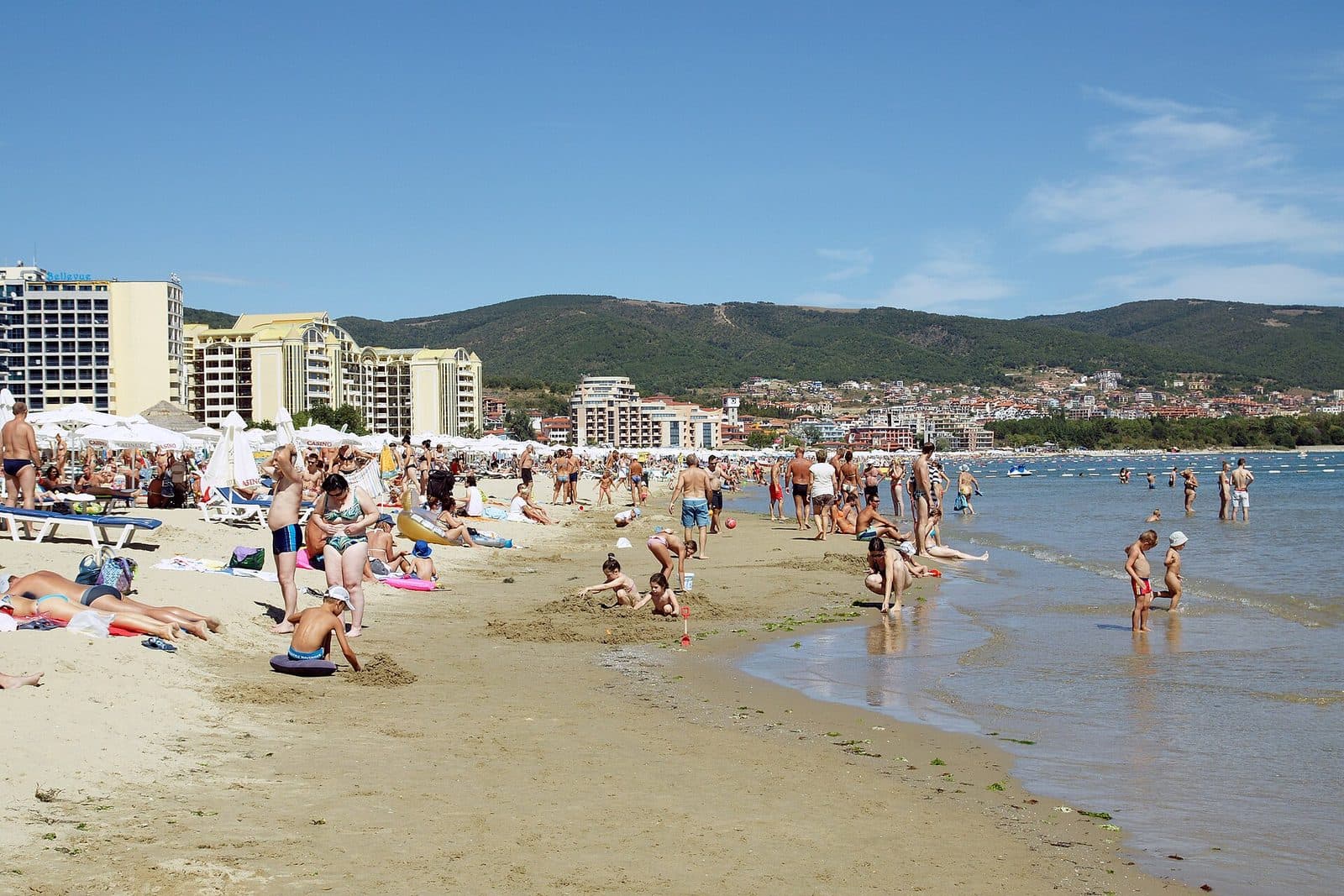 Holidaymakers on the long sandy beach at Sunny Beach, Bulgaria, with hotels and green hills behind